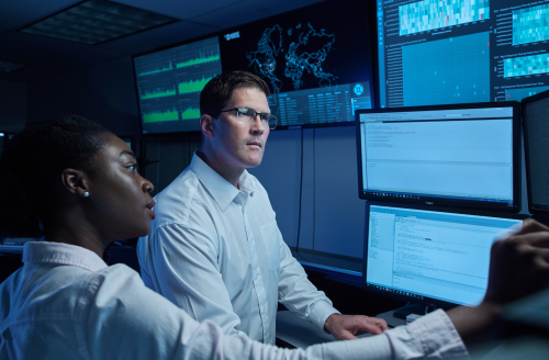Two programmers looking at multiple computer monitors