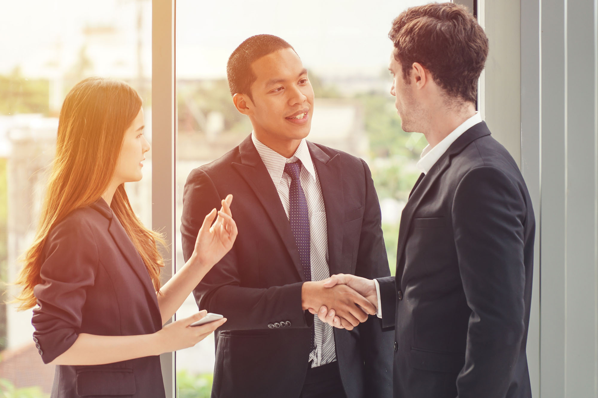 A vietnamese man shaking hands with a white man while a female in business attire is translating