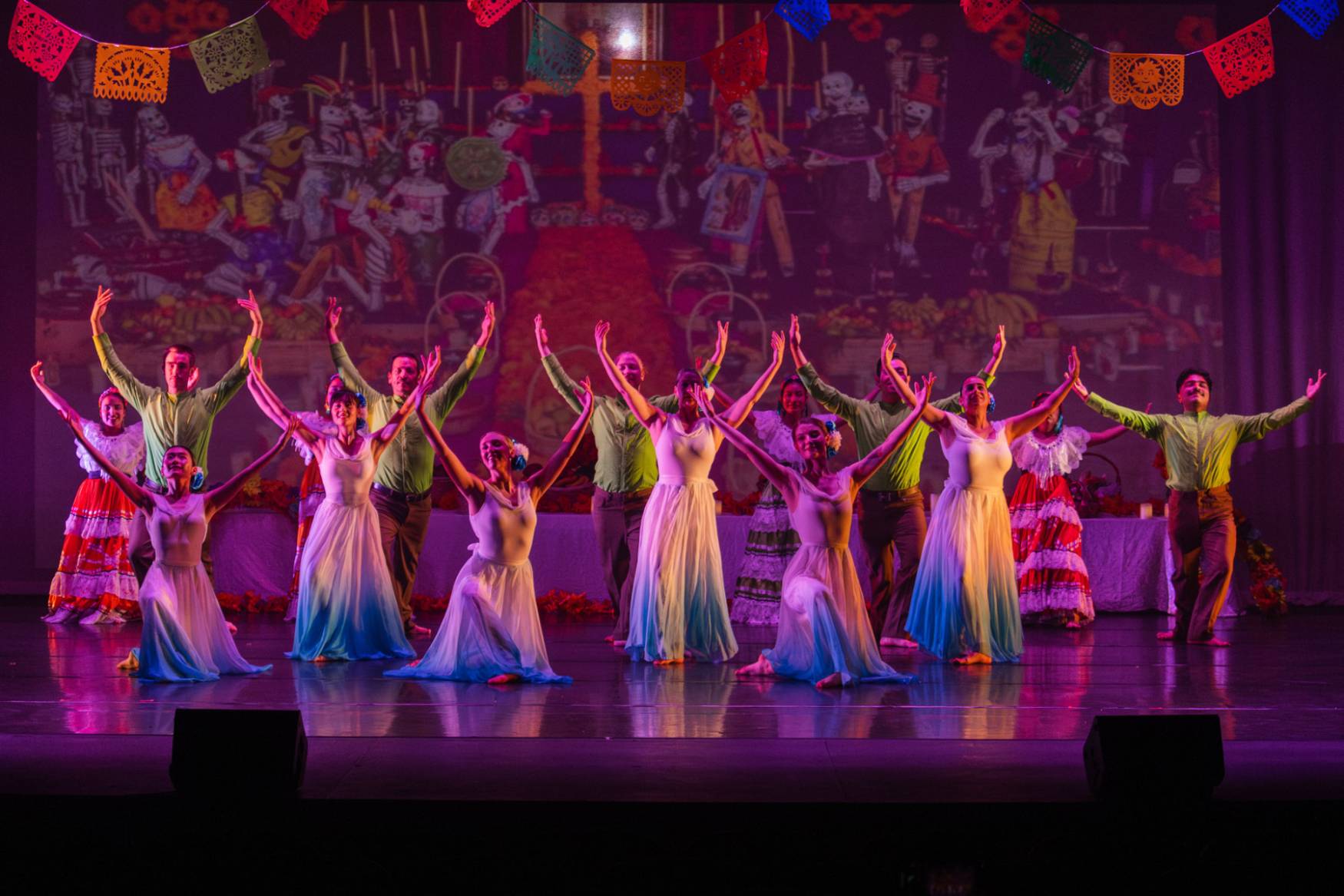 female dancers in gowns raising their arms in front of Dia De Los Muertos inspired mural
