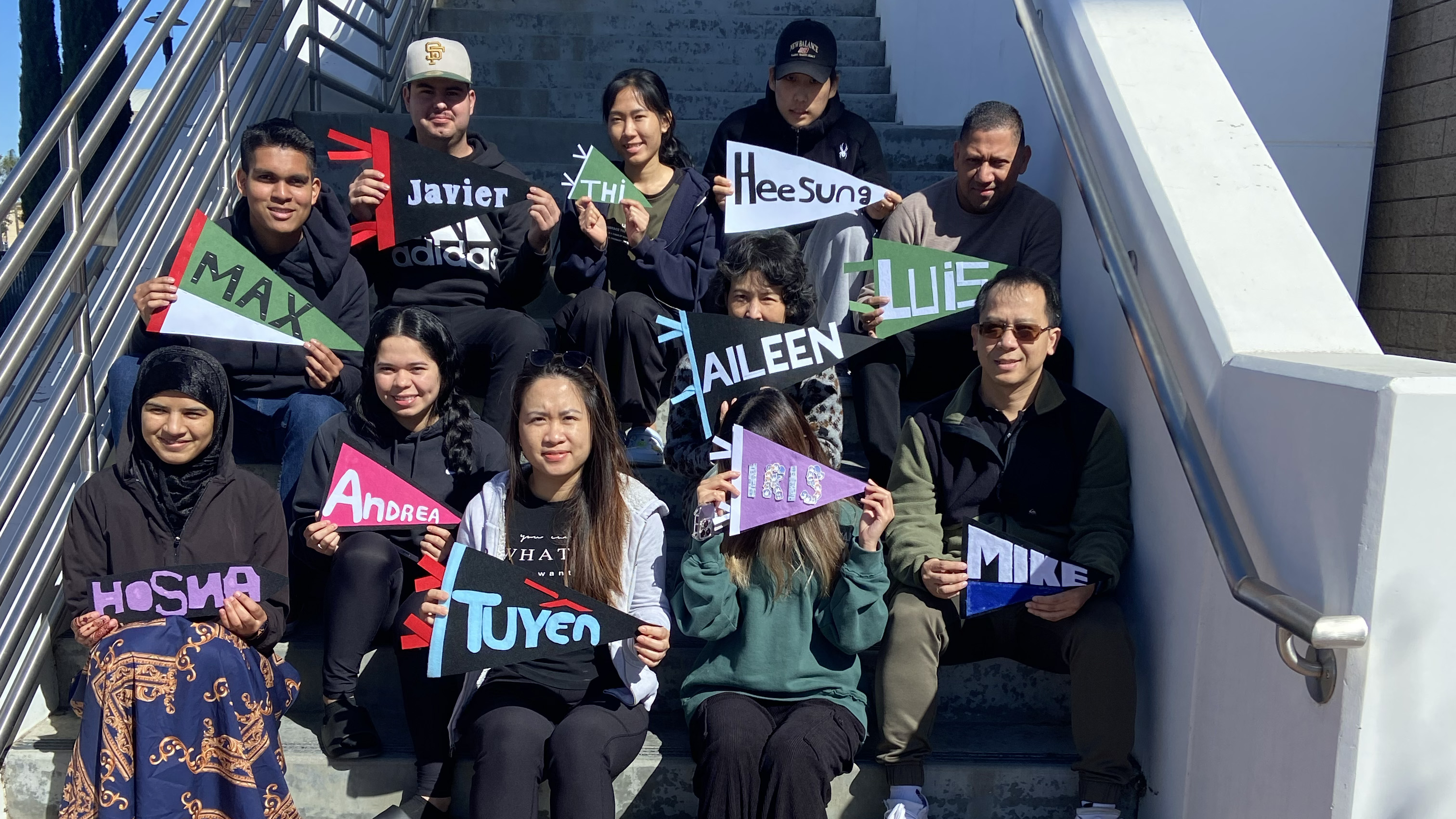 students seated on staircase holding up banners that have their names