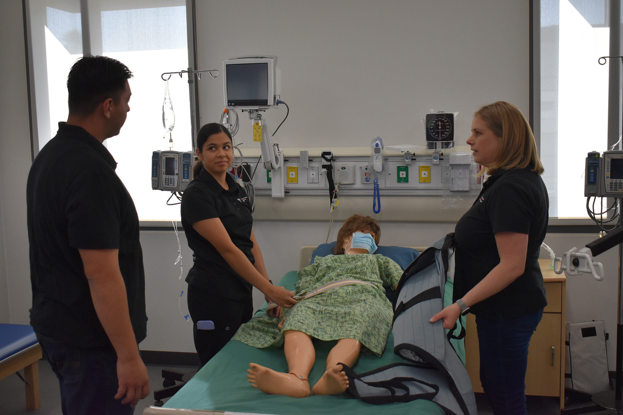 Three OTA students practicing rehab on a dummy patient